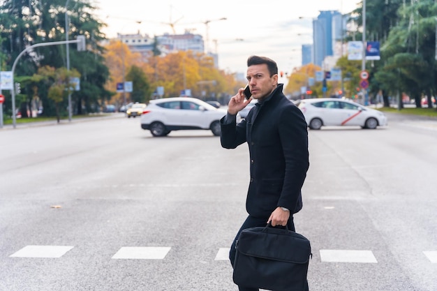 Uomo d'affari caucasico di mezza età che parla al telefono che attraversa la strada in città