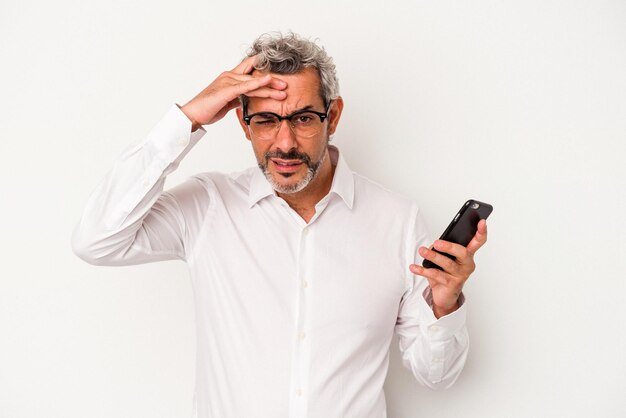 Uomo d'affari caucasico di mezza età in possesso di un telefono cellulare isolato su sfondo bianco scioccato che ha ricordato un incontro importante