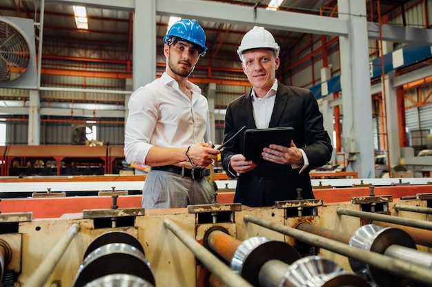 Uomo d'affari caucasico e ingegnere di fabbrica che parlano e discutono presso la produzione dell'industria pesante Operaio in elmetto protettivo di sicurezza presso le strutture industriali della fabbrica