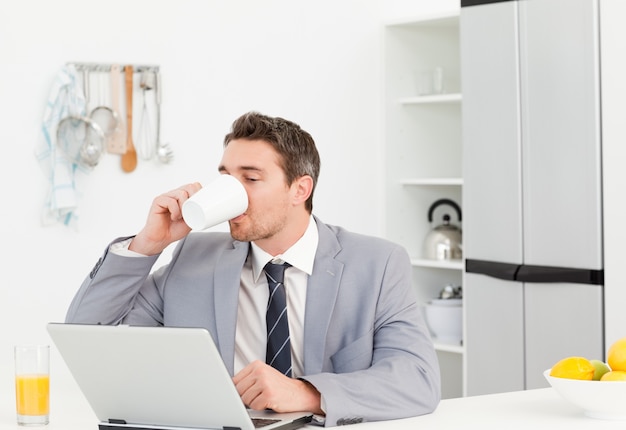 Uomo d&#39;affari che beve mentre sta guardando il suo computer portatile