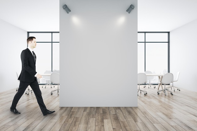 Uomo d'affari che cammina nella sala conferenze con un muro bianco vuoto