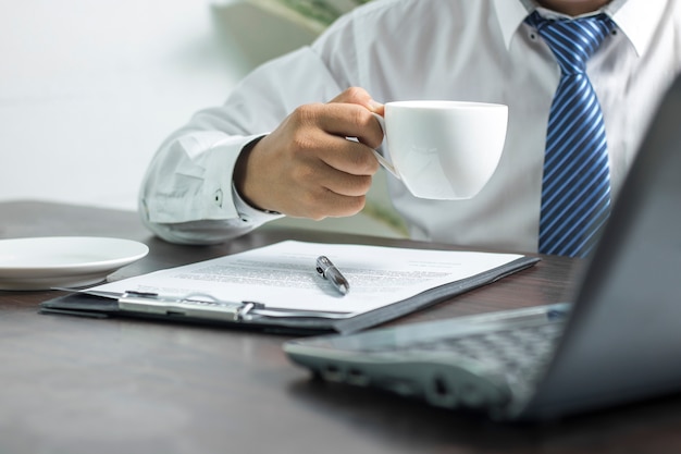 uomo d&#39;affari che considera computer e che tiene tazza di caffè