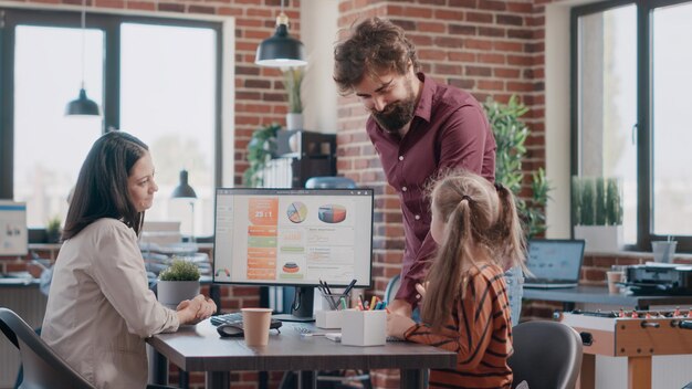 Uomo d'affari che disegna con il bambino sul taccuino mentre la donna lavora al computer in ufficio. Progetto di pianificazione della madre che lavora e figlia che giocano e scarabocchiano con il collega sul posto di lavoro