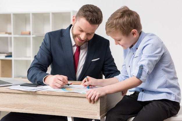 Uomo d'affari che disegna su documenti di lavoro con il figlio in ufficio