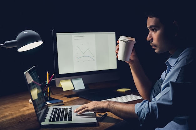 Uomo d'affari che fa gli straordinari a tarda notte nell'ufficio che si concentra sul lavoro con il computer portatile