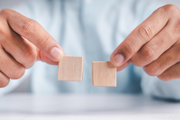 Uomo d'affari che indossa una camicia blu che dispone i blocchi di legno vuoti con le mani che è posizionato su un tavolo di legno bianco Strategia aziendale e piano d'azione Spazio di copia