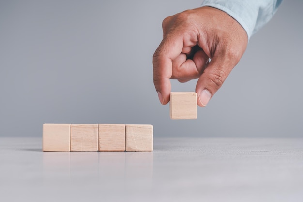 Uomo d'affari che indossa una camicia blu che dispone i blocchi di legno vuoti con le mani che è posizionato su un tavolo di legno bianco Strategia aziendale e piano d'azione Spazio di copia