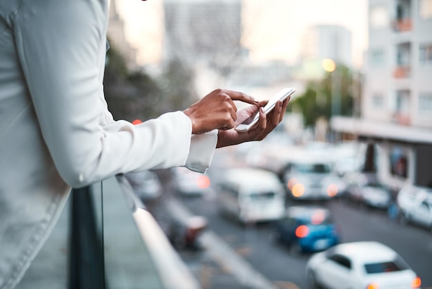 Uomo d'affari che invia un messaggio sul cellulare per inviare un'e-mail all'esterno sul balcone di un ufficio moderno che si affaccia su una città frenetica Lavoratore professionista aziendale che digita all'aperto per inviare un messaggio di testo