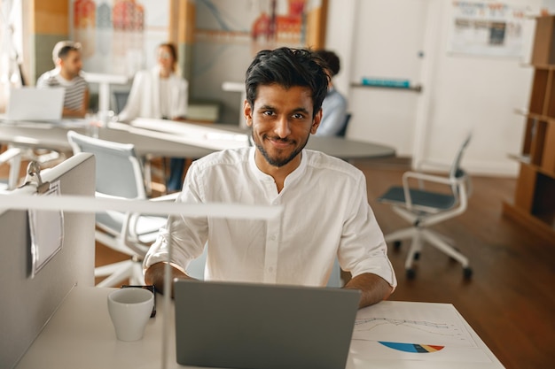 Uomo d'affari che lavora al computer portatile mentre è seduto in un ufficio moderno sullo sfondo dei colleghi