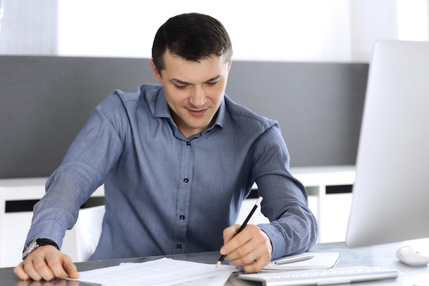 Uomo d'affari che lavora con il computer in un ufficio moderno. Colpo di testa dell'imprenditore maschio o del direttore dell'azienda sul posto di lavoro. Concetto di affari.