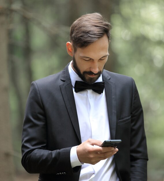 Uomo d'affari che legge SMS sullo smartphone in piedi nel bosco.