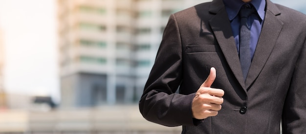 Uomo d&#39;affari che mostra i pollici su con il fondo all&#39;aperto della città