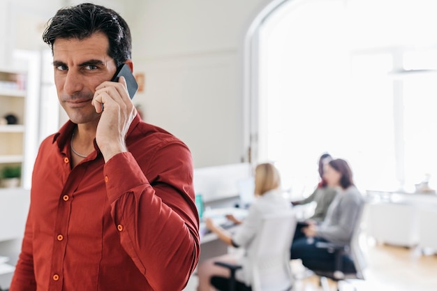 Uomo d'affari che parla al telefono in ufficio con i colleghi che lavorano in background