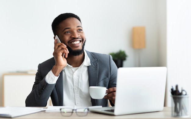 Uomo d'affari che parla sul cellulare e beve caffè sul posto di lavoro