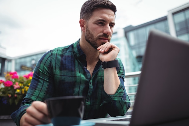 Uomo d'affari che per mezzo del computer portatile mentre mangiando una tazza di caffè