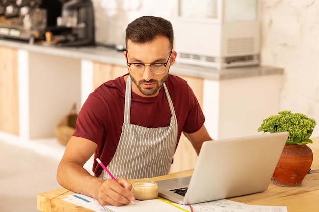 Uomo d'affari che possiede una caffetteria che lavora al computer portatile e prende appunti