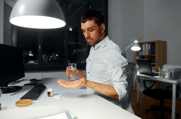 uomo d'affari che prende pillole di medicina in ufficio notturno