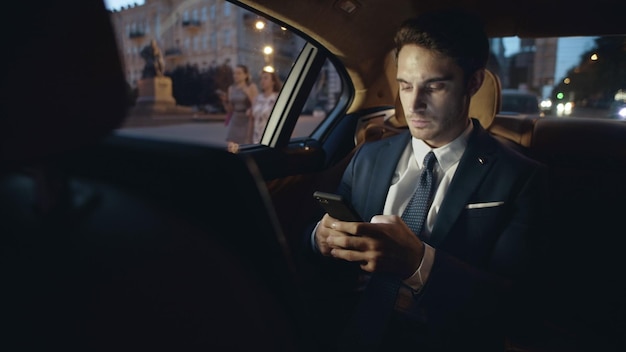 Uomo d'affari che scrive un messaggio sullo smartphone in auto Uomo che digita il testo sul cellulare