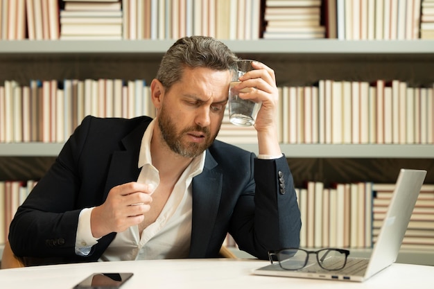 Uomo d'affari che soffre di mal di testa dopo il lavoro al computer esaurito con gli occhi chiusi che toccano la testa re