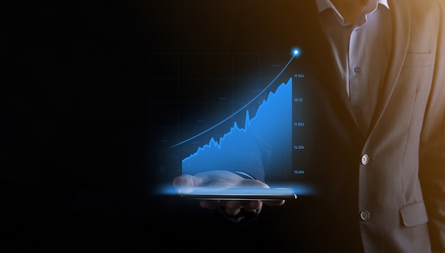 Uomo d'affari che tiene e mostra grafici olografici e statistiche del mercato azionario guadagna profitti Concetto di pianificazione della crescita e strategia aziendale Visualizzazione di una buona economia sotto forma di schermo digitale