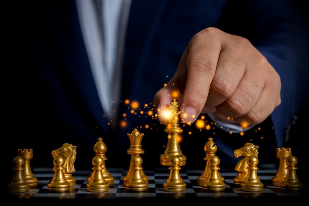 Uomo d'affari che tiene in mano un brillante scacchi d'oro per utilizzare la strategia aziendale dei concorrenti per la vittoria futura