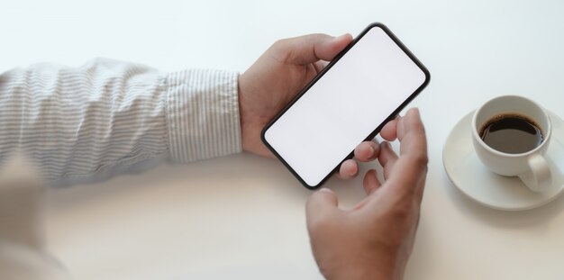 Uomo d'affari che tiene lo smartphone dello schermo in bianco nell'area di lavoro comoda