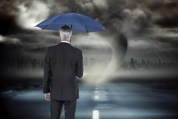 Uomo d'affari che tiene ombrello contro il cielo tempestoso con tornado su strada