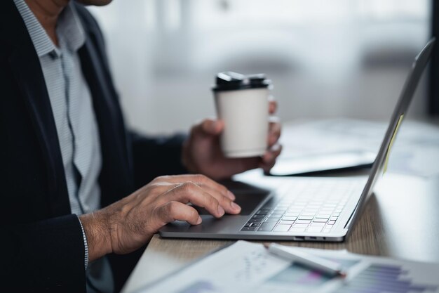 Uomo d'affari che tiene una tazza di caffè caldo e lavora al computer portatile sul tavolo di legno a casa Donna imprenditrice che lavora per la sua attività a casa Concetto di lavoro a casa