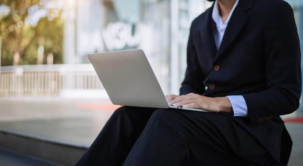 Uomo d'affari che trasporta una borsa per laptop e fa affari fuori e lavora su un tablet portatile mentre è seduto in strada urbana