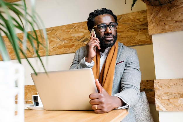 Uomo d'affari che usa telefono e laptop al tavolo in un caffè