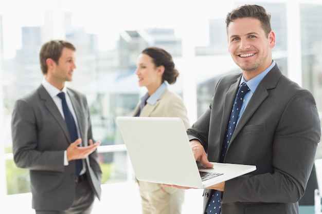 Uomo d&#39;affari che utilizza computer portatile con i colleghi che discutono nell&#39;ufficio