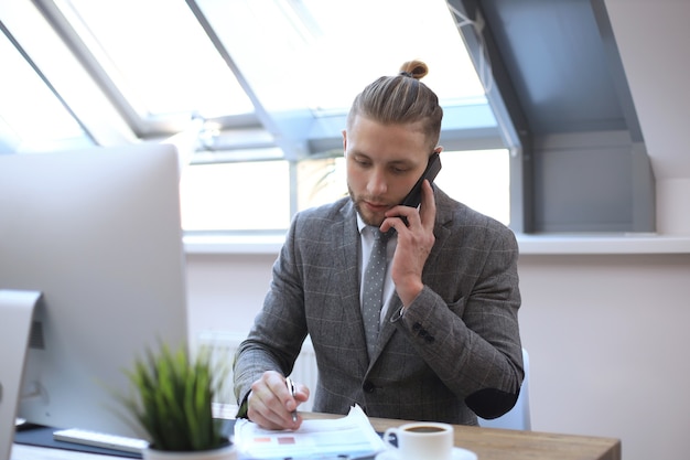 Uomo d'affari che utilizza il suo telefono cellulare in ufficio.