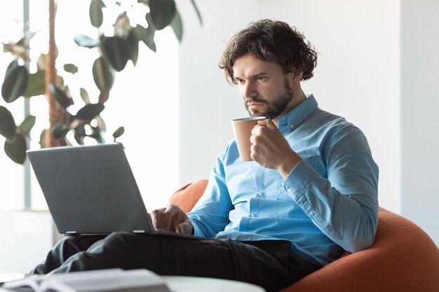 Uomo d'affari che utilizza pc seduto sulla sedia a bere caffè