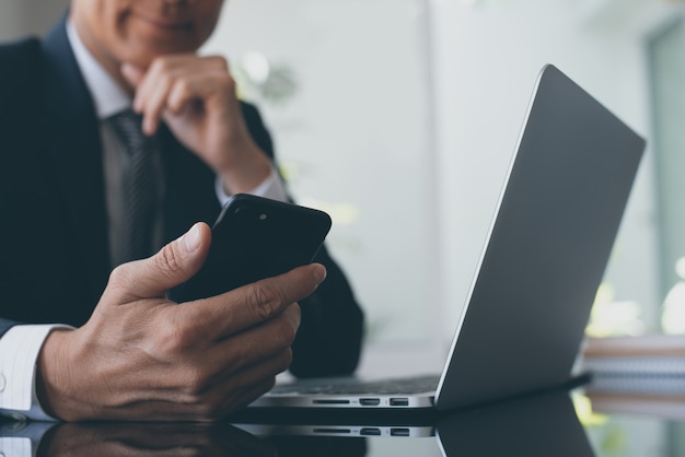 Uomo d'affari che utilizza smartphone mentre lavorando al computer portatile nell'ufficio