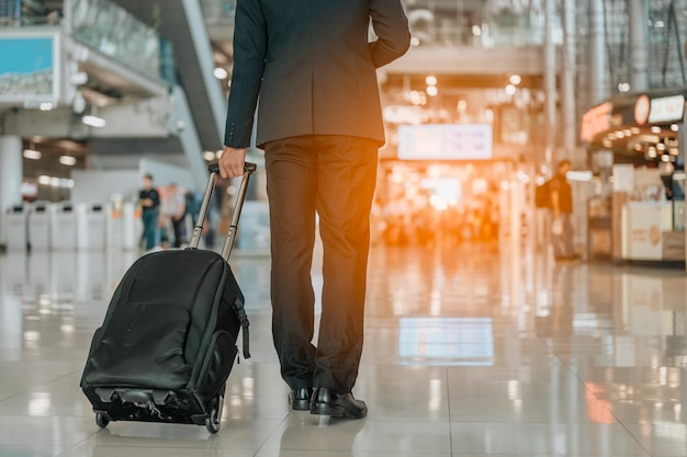 Uomo d'affari con bagaglio a mano che cammina nel terminal dell'aeroporto. Uomo d'affari che trasporta la valigia mentre si cammina attraverso un terminal di partenza dei passeggeri in aeroporto. Viaggio d'affari di viaggio del viaggiatore dell'uomo d'affari.