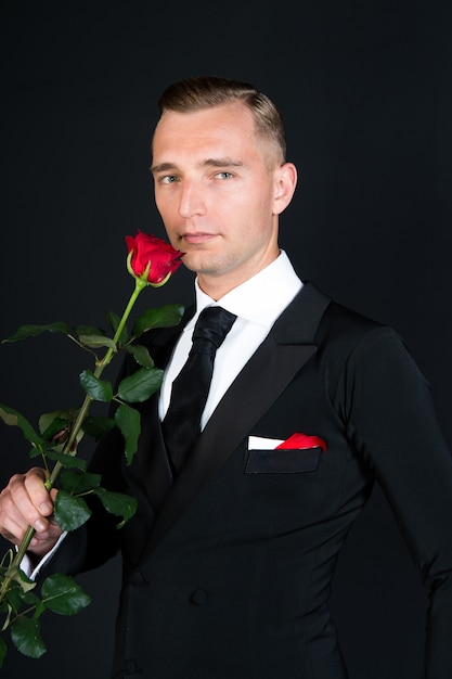 Uomo d'affari con fiore di rosa rossa su sfondo nero, concetto di amore romantico di San Valentino