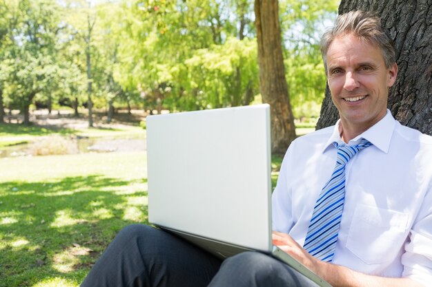 Uomo d&#39;affari con il computer portatile che si appoggia sul tronco d&#39;albero