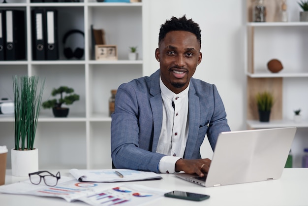 Uomo d'affari con il portatile. Il giovane uomo d'affari africano sta scrivendo qualcosa sul computer portatile nel suo ufficio.