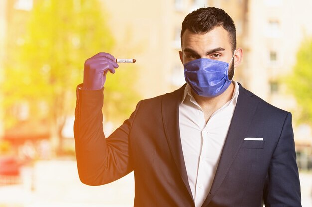 Uomo d'affari con maschera chirurgica e guanti che tiene una provetta per analisi del sangue che è firmata come negativa Covid-19