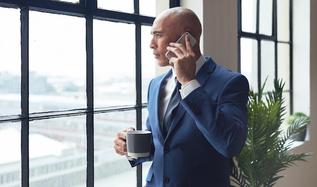 Uomo d'affari con telefonata pausa caffè e comunicazione in ufficio CEO e networking con negoziazione Guarda fuori dalla finestra banchiere di investimento con affare finanziario di conversazione e professionale