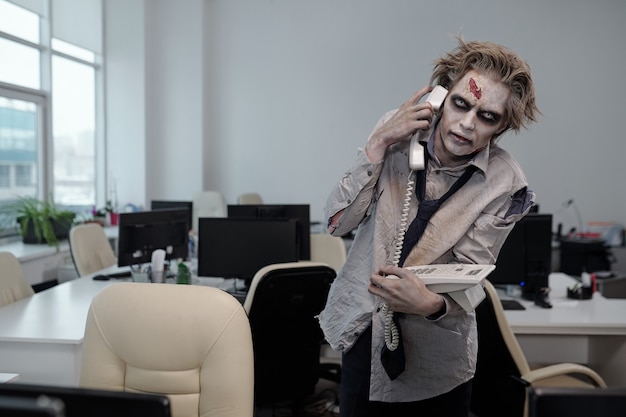 Uomo d'affari con trucco zombie che parla al telefono in un ambiente d'ufficio