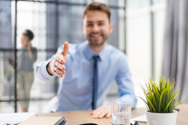 Uomo d'affari con una mano aperta pronta a sigillare un accordo in ufficio con i colleghi sullo sfondo