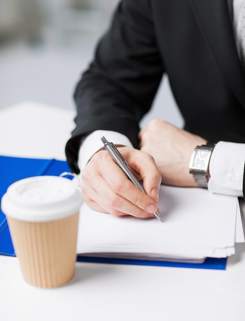 uomo d'affari con una tazza di caffè che scrive qualcosa sulla carta