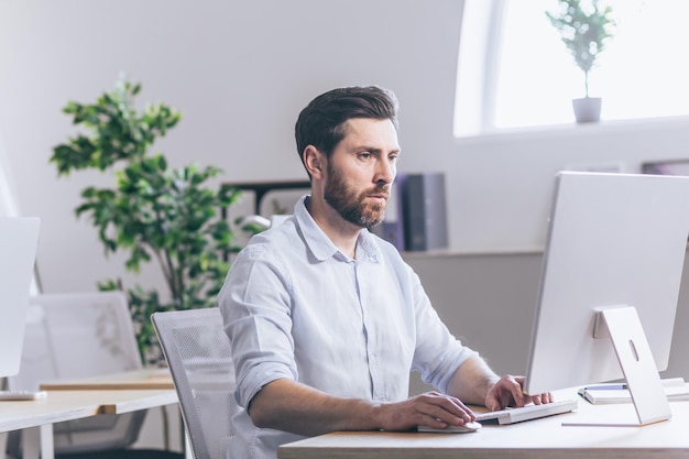 Uomo d'affari concentrato e pensieroso che lavora in ufficio presso l'uomo del broker di scartoffie del computer che guarda il monitor