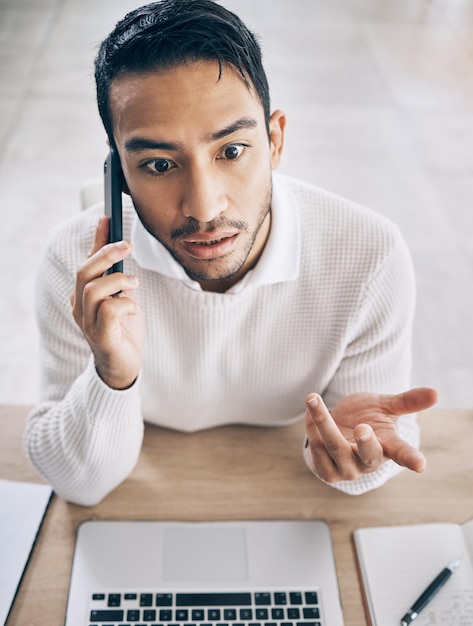 Uomo d'affari confuso e telefonata con conversazione sul laptop e in ufficio Cellulare maschio asiatico e parlando per una società di avvio sconvolta per problemi di affare e comunicazione smartphone e vista dall'alto