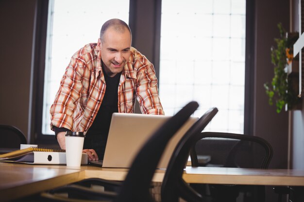 Uomo d'affari creativo che per mezzo del computer portatile mentre appoggiandosi allo scrittorio