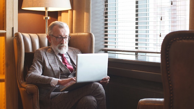 Uomo d'affari dai capelli grigi elegante che si siede al computer portatile