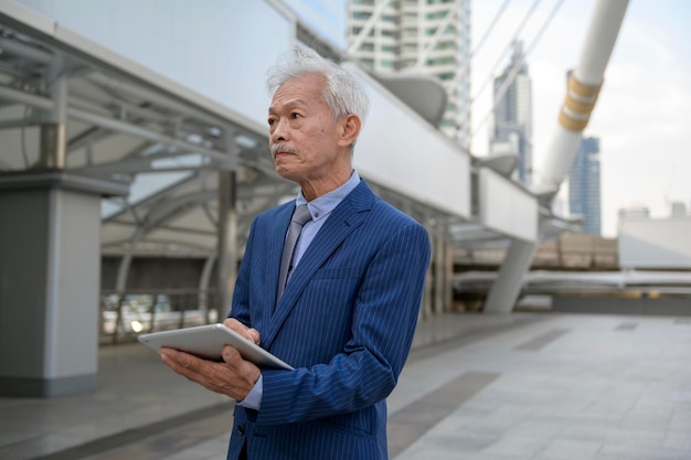 Uomo d'affari di mezza età anziano maturo asiatico utilizzando tablet nella città moderna