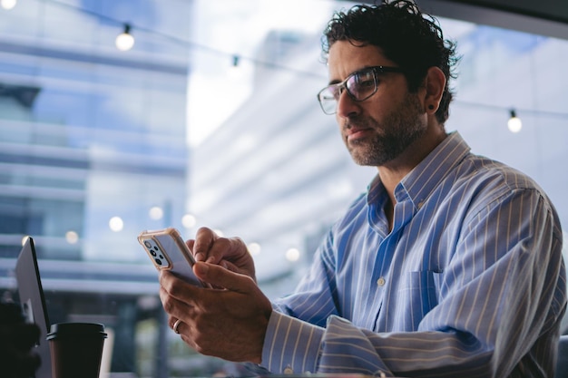 Uomo d'affari di mezza età in una caffetteria che ingrandisce l'immagine di un telefono cellulare