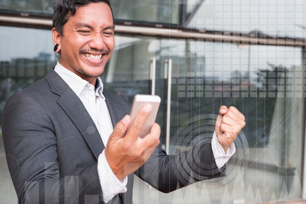 Uomo d'affari di successo che controlla il messaggio del cellulare e che gesturing con felicità e letizia